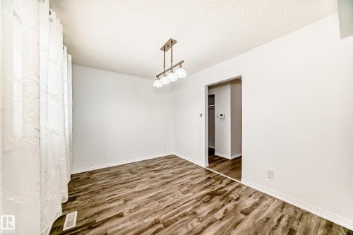 This room features light-toned walls, wood-style flooring, a decorative chandelier, and white sheer curtains - 4312 43 Avenue, Leduc, AB - Indoor Photo Showing Other Room