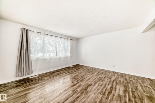 This room features wood-look flooring and a window with sheer curtains, providing a view of outdoor trees - 4312 43 Avenue, Leduc, AB - Indoor Photo Showing Other Room