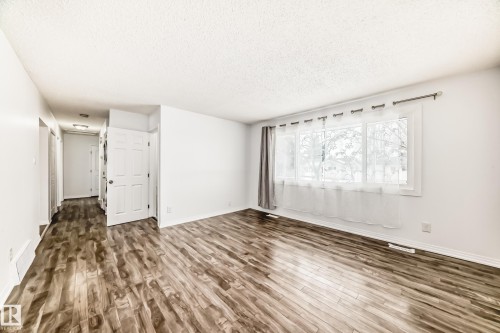 Bright living area featuring wood-look flooring and a large window with sheer white curtains - 4312 43 Avenue, Leduc, AB - Indoor Photo Showing Other Room