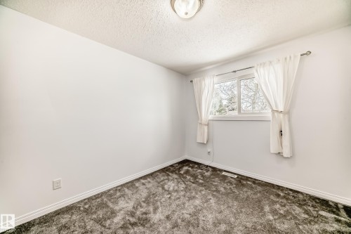 The room features white walls, dark carpet flooring, and a window with white curtains - 4312 43 Avenue, Leduc, AB - Indoor Photo Showing Other Room