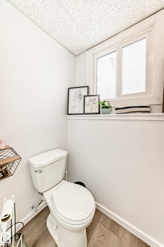 This bathroom features wood-style flooring, a white toilet, and a window with white trim - 4312 43 Avenue, Leduc, AB - Indoor Photo Showing Bathroom