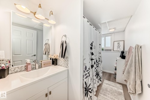 This bathroom features a white vanity with an integrated sink, a large mirror, and a gold-toned light fixture - 4312 43 Avenue, Leduc, AB - Indoor Photo Showing Bathroom