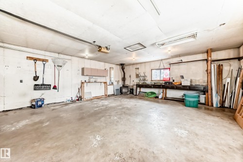 The property features a spacious garage with a concrete floor, built-in shelving, and overhead lighting - 4312 43 Avenue, Leduc, AB - Indoor Photo Showing Garage