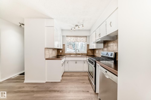 The kitchen features white cabinetry, stainless steel appliances including a range and dishwasher, and a tiled backsplash - 4312 43 Avenue, Leduc, AB - Indoor Photo Showing Kitchen With Double Sink