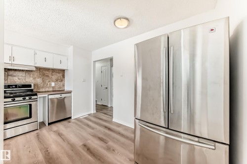 The kitchen features white cabinetry, stainless steel appliances including a refrigerator, range, and dishwasher, and a tiled backsplash - 4312 43 Avenue, Leduc, AB - Indoor Photo Showing Kitchen