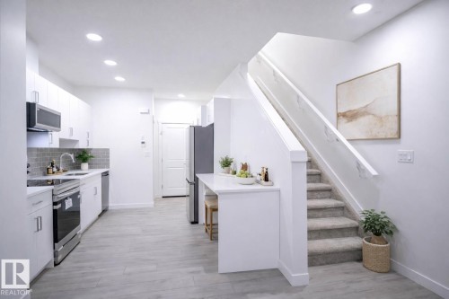 Virtually Staged Kitchen with stainless steel appliances, white cabinets, light wood-style flooring, decorative backsplash, and recessed lighting - 53 7110 Keswick Common Sw, Edmonton, AB - Indoor Photo Showing Kitchen