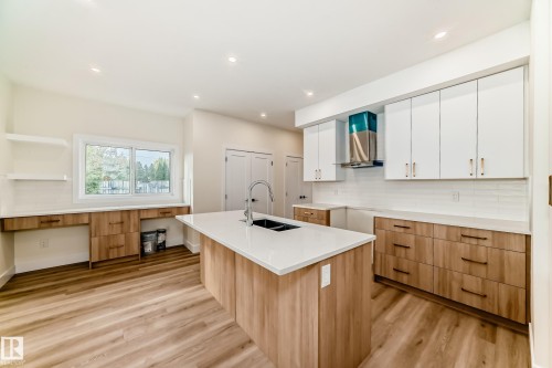 The kitchen features a large island with a sink, light wood cabinetry with dark handles, and a white subway tile backsplash - 10718 149 Street Nw, Edmonton, AB - Indoor Photo Showing Kitchen With Double Sink