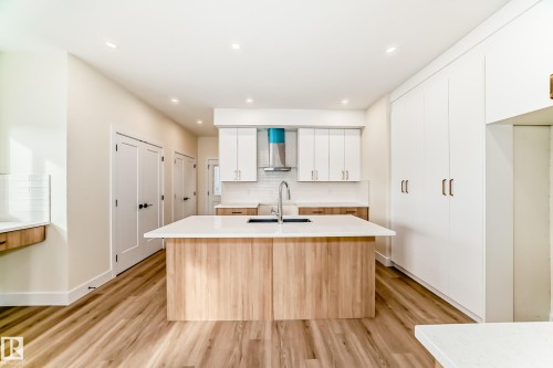 The kitchen features a large island with a sink, white countertops, a tiled backsplash, and recessed lighting - 10718 149 Street Nw, Edmonton, AB - Indoor Photo Showing Kitchen