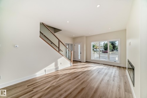 The living area features light wood-style flooring, a staircase with a glass panel railing and wood handrail, and large windows - 10718 149 Street Nw, Edmonton, AB - Indoor Photo Showing Other Room