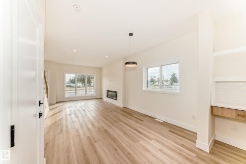 This bright living area features light wood flooring, a modern fireplace, and large windows that provide abundant natural light - 10718 149 Street Nw, Edmonton, AB - Indoor