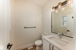 This powder room features a white vanity with a rectangular sink, a chrome faucet, and a large mirror with a black frame - 