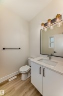 The bathroom features wood-look flooring, a white vanity with a light-colored countertop, and a vanity light fixture with four lights - 
