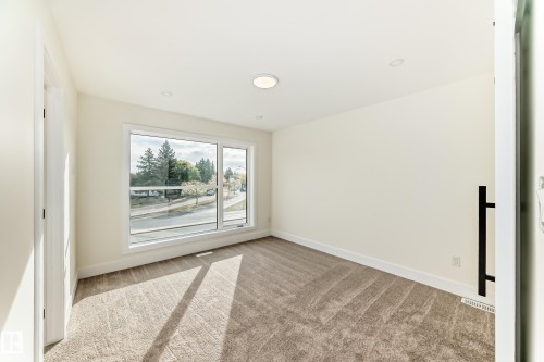 The room features a large window, providing natural light and views of the surrounding trees and street - 10718 149 Street Nw, Edmonton, AB - Indoor Photo Showing Other Room