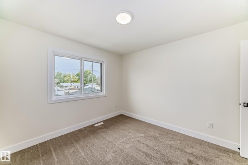 This room features light-colored walls, a window providing a view of surrounding structures and trees, and a ceiling light fixture - 10718 149 Street Nw, Edmonton, AB - Indoor Photo Showing Other Room