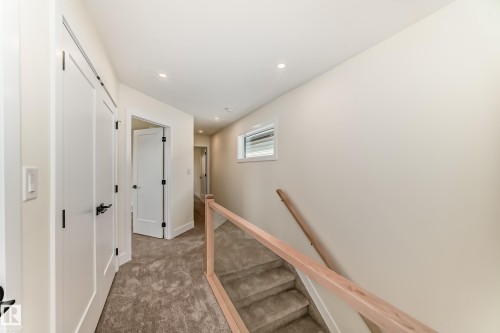 Hallway featuring light-colored walls, recessed lighting, and a staircase with a wooden handrail and glass panels - 10718 149 Street Nw, Edmonton, AB - Indoor Photo Showing Other Room