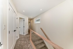 Hallway featuring light-colored walls, recessed lighting, and a staircase with a wooden handrail and glass panels - 