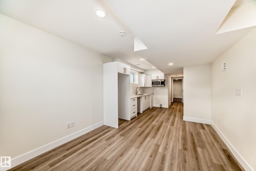 Open concept living area featuring wood-look flooring, recessed lighting, and a kitchen area with white cabinetry and a built-in microwave - 10718 149 Street Nw, Edmonton, AB - Indoor