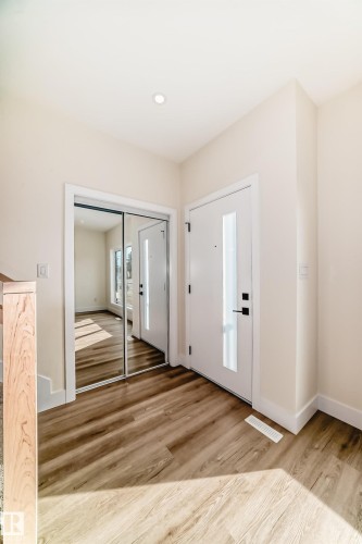 The entryway features light-toned wood-style flooring, a white modern door with a rectangular window, and a mirrored closet door - 10718 149 Street Nw, Edmonton, AB - Indoor Photo Showing Other Room