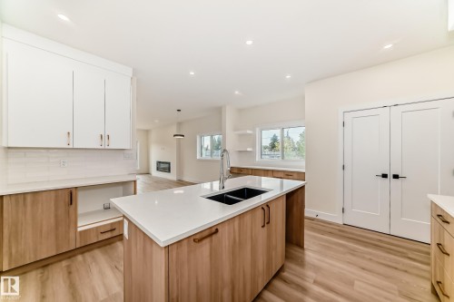 Bright kitchen featuring a central island with a double basin sink, white countertops, and light wood cabinetry - 10718 149 Street Nw, Edmonton, AB - Indoor Photo Showing Kitchen With Double Sink