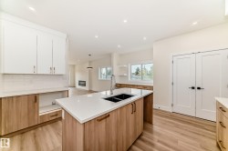 Bright kitchen featuring a central island with a double basin sink, white countertops, and light wood cabinetry - 