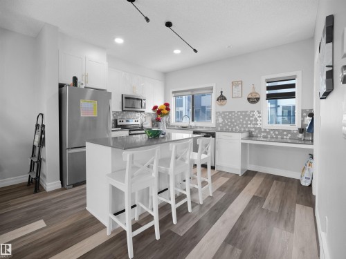 The kitchen features white cabinetry, stainless steel appliances, and a central island with bar seating - 138 804 Welsh Drive, Edmonton, AB - Indoor Photo Showing Kitchen