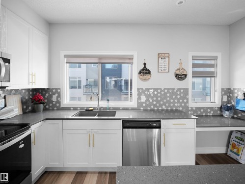 The kitchen features white cabinetry with gold-toned hardware, a stainless steel dishwasher, and a dual basin sink - 138 804 Welsh Drive, Edmonton, AB - Indoor Photo Showing Kitchen With Double Sink