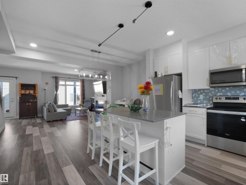 Open concept living area featuring a kitchen island with seating, a living room with a window, and wood-look flooring throughout - 138 804 Welsh Drive, Edmonton, AB - Indoor Photo Showing Kitchen With Upgraded Kitchen