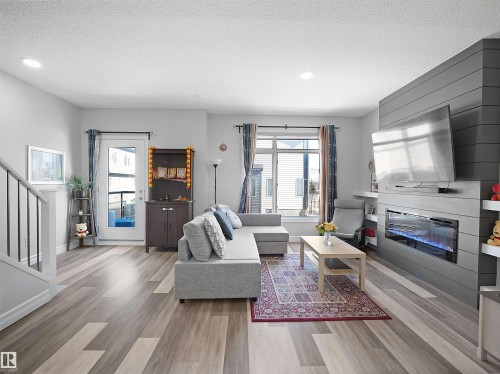 Spacious living area featuring light wood-style flooring, a large window, and a built-in fireplace with a media console - 138 804 Welsh Drive, Edmonton, AB - Indoor Photo Showing Living Room With Fireplace