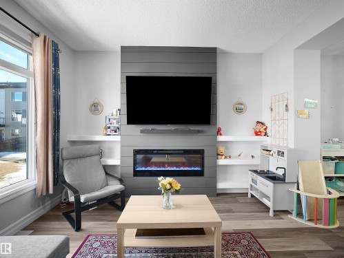 Living area featuring light wood flooring, a decorative fireplace, and built-in shelving - 138 804 Welsh Drive, Edmonton, AB - Indoor Photo Showing Living Room With Fireplace