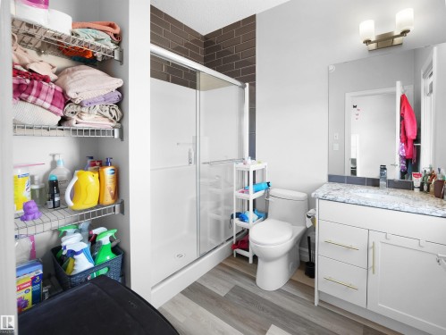 This bathroom features a shower with dark tiled walls, a vanity with a light-colored countertop and a mirror, and wood-style flooring - 138 804 Welsh Drive, Edmonton, AB - Indoor Photo Showing Bathroom