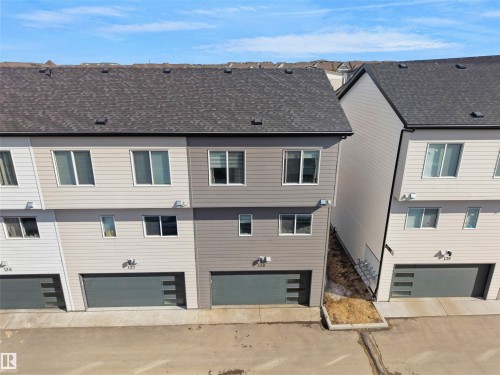 This property features a contemporary exterior with multi-toned siding, a dark shingled roof, and an integrated garage with a modern style door - 138 804 Welsh Drive, Edmonton, AB - Outdoor