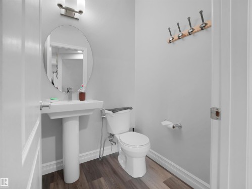 This bathroom features a pedestal sink with a contemporary faucet, an oval mirror, and dark-toned flooring - 138 804 Welsh Drive, Edmonton, AB - Indoor Photo Showing Bathroom