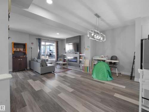 Spacious living area featuring light-toned flooring, a large window, recessed lighting, and a modern light fixture - 138 804 Welsh Drive, Edmonton, AB - Indoor
