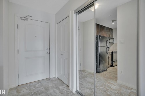 The property features a white paneled door, light-colored tile flooring, and a mirrored closet door - 108 1204 156 Street, Edmonton, AB - Indoor Photo Showing Other Room