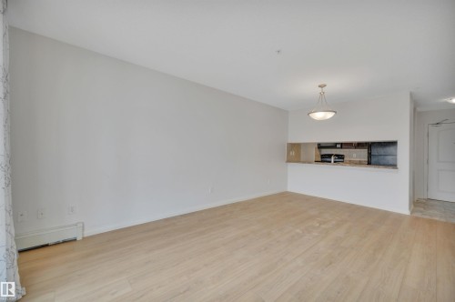 Spacious open concept living area featuring light wood flooring, a pass-through window to the kitchen, and a ceiling light fixture - 108 1204 156 Street, Edmonton, AB - Indoor