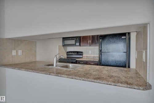 The kitchen features a double basin sink with a chrome faucet, dark wood cabinetry, and a black refrigerator - 108 1204 156 Street, Edmonton, AB - Indoor Photo Showing Kitchen With Double Sink