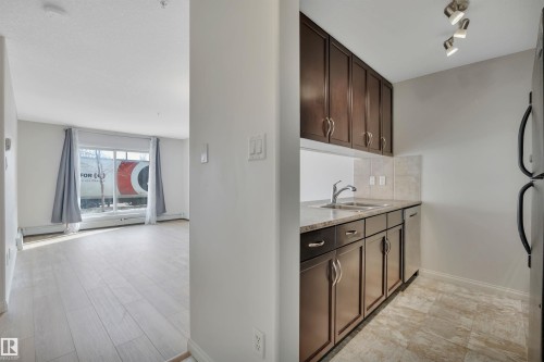 The kitchen features dark wood cabinetry, a double basin sink, and stainless steel appliances - 108 1204 156 Street, Edmonton, AB - Indoor Photo Showing Kitchen With Double Sink