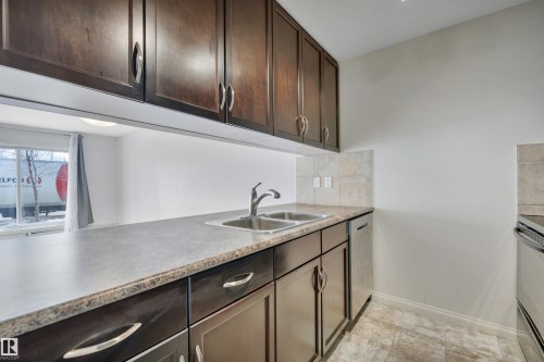 The kitchen features dark wood cabinetry, a double basin stainless steel sink with a chrome faucet, and tiled countertops - 108 1204 156 Street, Edmonton, AB - Indoor Photo Showing Kitchen With Double Sink