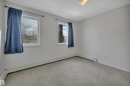 This room features light grey carpeting, white walls, and two windows providing natural light - 108 1204 156 Street, Edmonton, AB - Indoor Photo Showing Other Room