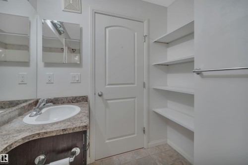 Bathroom featuring a single vanity with an integrated sink, a large mirror, and built-in shelving - 108 1204 156 Street, Edmonton, AB - Indoor