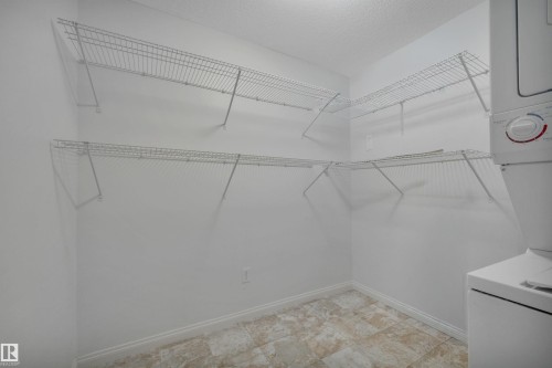 This utility room features white wire shelving, a tiled floor, and a stacked washer and dryer unit - 108 1204 156 Street, Edmonton, AB - Indoor With Storage