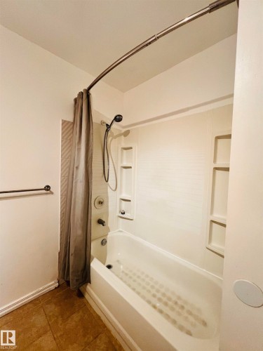 The bathroom features a white bathtub with an integrated shower, tiled flooring, and a towel bar - 11459 51 Avenue, Edmonton, AB - Indoor Photo Showing Bathroom