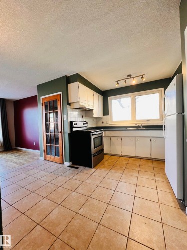 The kitchen features white cabinetry, a tiled backsplash, and light-colored tiled flooring - 11459 51 Avenue, Edmonton, AB - Indoor Photo Showing Kitchen