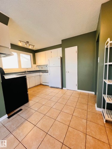 The kitchen features tile flooring, white cabinetry, a white refrigerator, and a black range - 11459 51 Avenue, Edmonton, AB - Indoor Photo Showing Kitchen