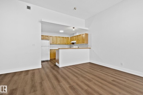 The property features an open-concept living area with wood-look flooring and white walls - 116 11033 127 Street, Edmonton, AB - Indoor Photo Showing Kitchen