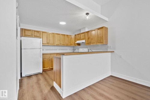 The kitchen features wood cabinetry, a white refrigerator, and a breakfast bar with a wooden countertop - 116 11033 127 Street, Edmonton, AB - Indoor Photo Showing Kitchen