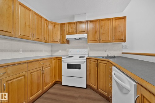 The kitchen features light wood cabinetry, white appliances, and a grey countertop with a tiled backsplash - 116 11033 127 Street, Edmonton, AB - Indoor Photo Showing Kitchen