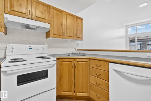 The kitchen features wooden cabinetry, white appliances, and a window providing natural light - 116 11033 127 Street, Edmonton, AB - Indoor Photo Showing Kitchen