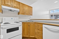 The kitchen features wooden cabinetry, white appliances, and a window providing natural light - 