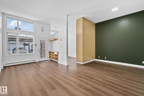 This room features light wood-style flooring, a floor-to-ceiling window, and a door with a window panel - 116 11033 127 Street, Edmonton, AB - Indoor Photo Showing Other Room